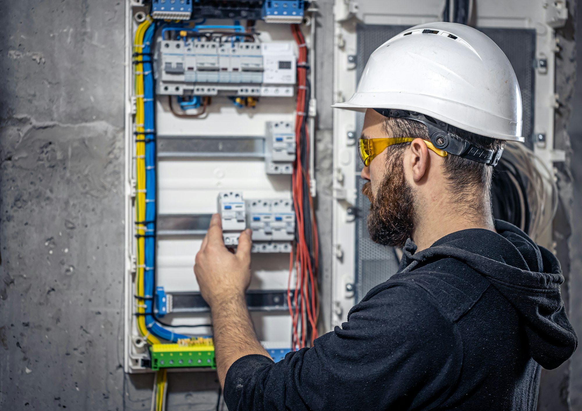 A male electrician works in a switchboard with an electrical connecting cable.
